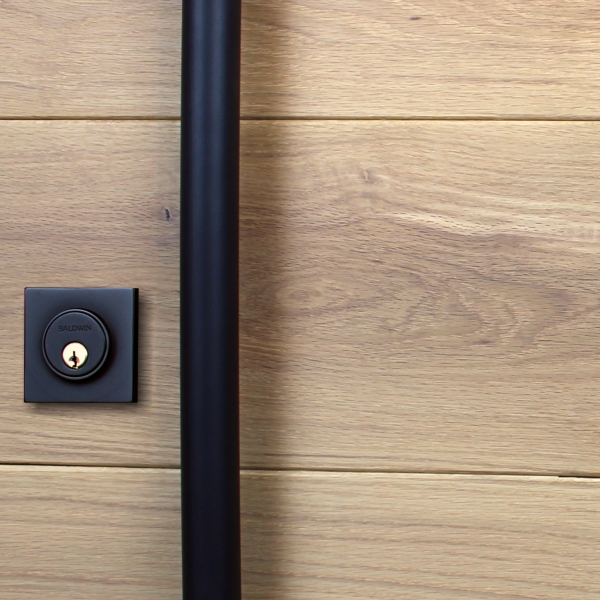 A wood pivot door with a black handle and matching black lock