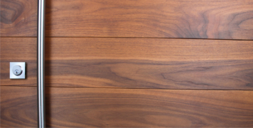 real walnut wood front door behind round stainless steel door pulls and baldwin square stainless steel door lock