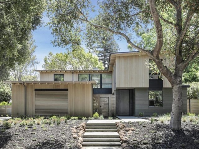 contemporary home with sloped roof, metal pivot door, wood accents, clean lines, and minimalist landscaping