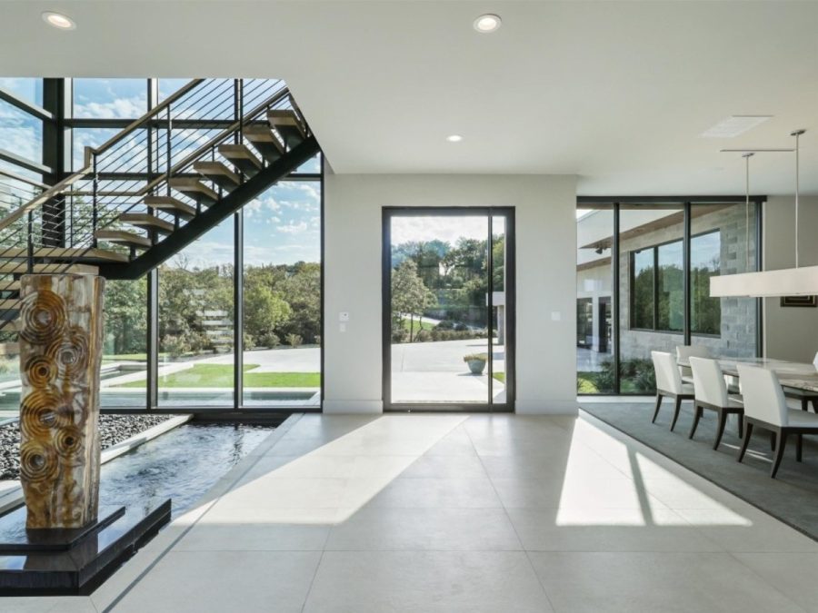 modern interior with glass pivot door, floating staircase, floor-to-ceiling windows, and an artistic indoor water feature