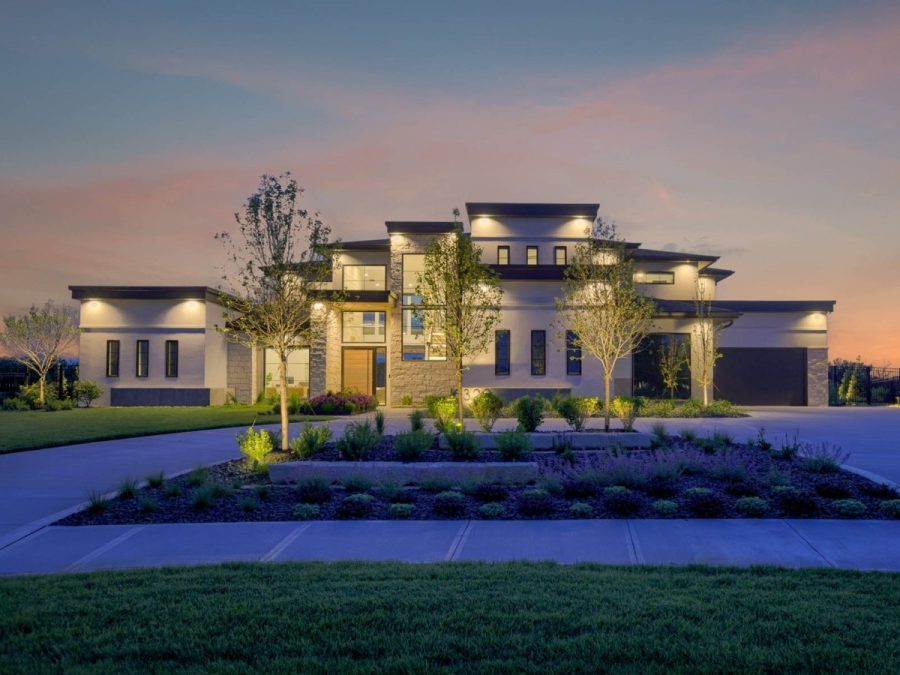 luxurious modern home with elegant facade, expansive windows, landscaped yard, and ambient nighttime lighting