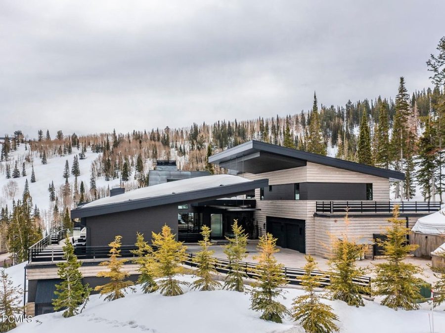 luxury ski lodge home with modern design, sloped roofs, mountain views, and snowy forest surroundings