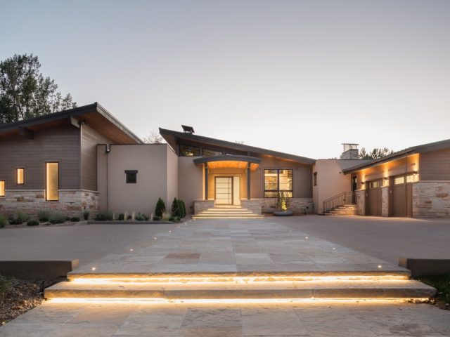 modern home with sloped roofs, warm exterior lighting, stone accents, and a grand illuminated entryway