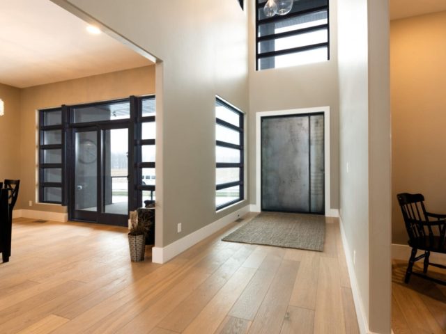 modern interior entryway with metal pivot door, large windows, natural light, and light wood flooring