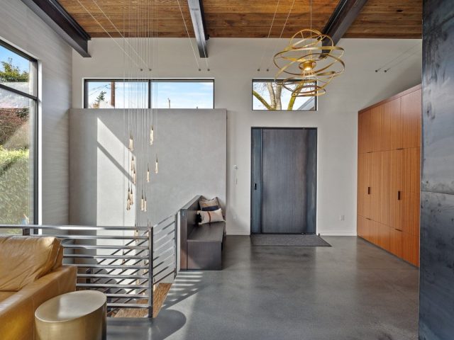 industrial-style entryway with raw steel pivot door, modern light fixture, large windows, and wood and concrete accents.
