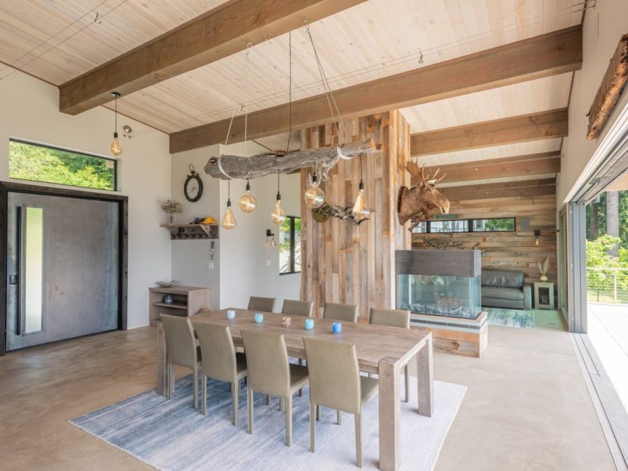 rustic dining area with wood beams, driftwood chandelier, reclaimed wood accents, and large windows overlooking nature