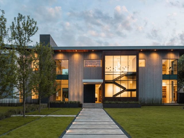 modern home with metal facade, black accents, floor-to-ceiling windows, landscaped yard, and illuminated walkway.
