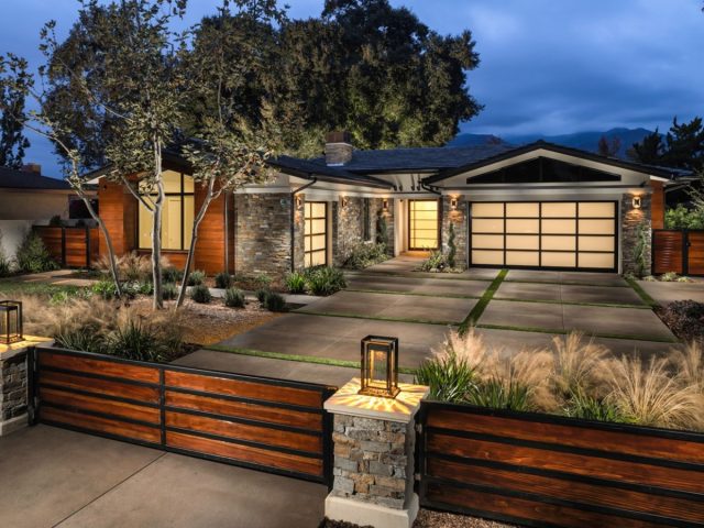 modern home exterior with stone and wood accents, frosted glass garage doors, landscaped yard, and warm outdoor lighting